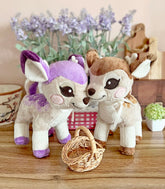 Lavendeer and Cinnafawn deer plush posing together with flowers and a wicker basket